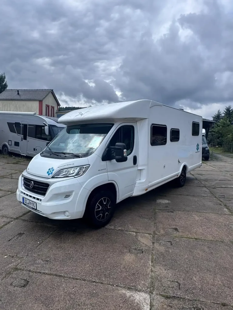 Weißes Wohnmobil frontal aufgenommen, auf gepflasterter Fläche.